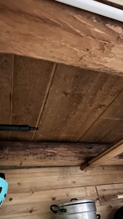 Tak i ett rum med synliga träpaneler och en stor kastrull i förgrunden. Rummet är tänkt för isolering med råd om att använda vindpapp.