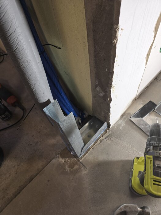 Vinkeljärn monterat vid golv och vägg, med borr och ventilationsrör i bakgrunden.