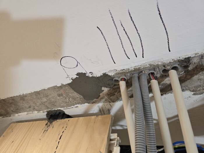 Vägg med installerade ventiler och kablage i ett rum under renovering. Märkningar på väggen och en träskiva i förgrunden.