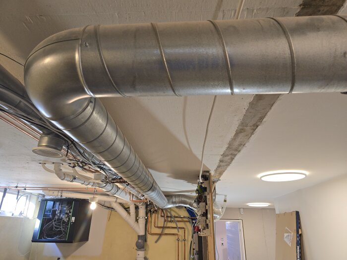 Ventilationsrör av stål monterade i taket i ett rum under renovering, med kablar och ledningar synliga i bakgrunden.