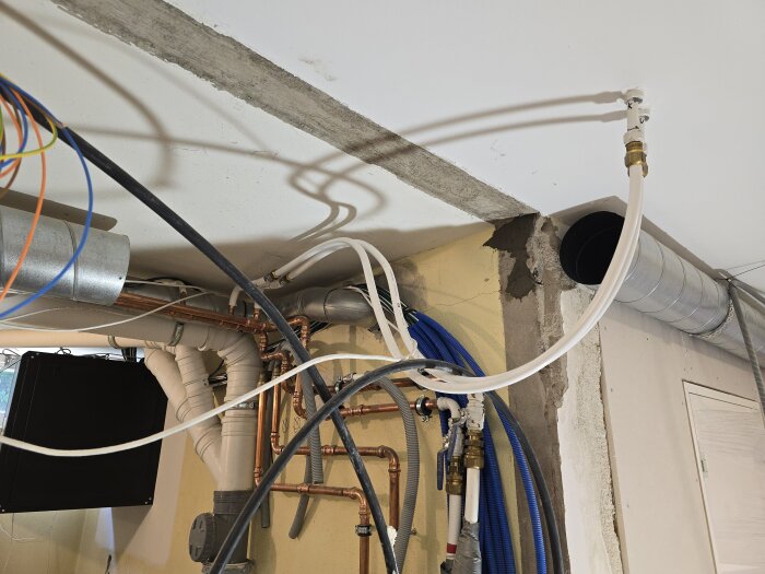 Takinstallation med stålreglar, ventilationsrör och elkablar. Exponerad betong och isolerade rör är synliga vid plats för ny vägg.