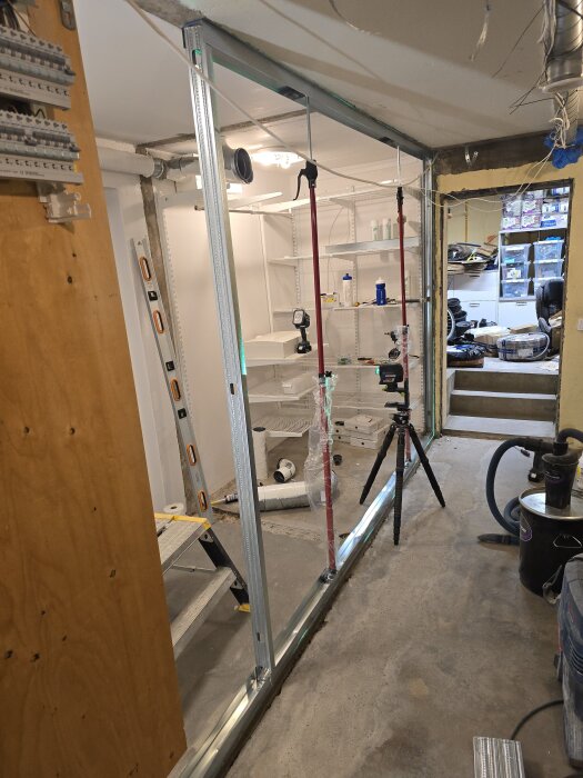 En halvfärdig innervägg med stålskenor och verktyg som vattenpass, borrmaskin och dammsugare i ett renoveringsprojekt.