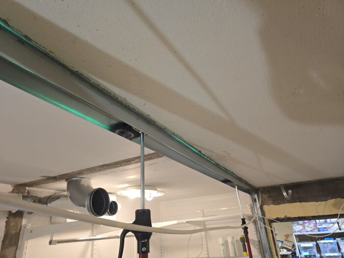 Takmonterad stålregel med borrstång under installation, ventilation synlig i bakgrunden, inom ett renoveringsprojekt.