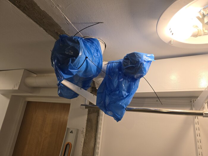 Blå plastpåsar skyddar ventilationsrör i taket under byggarbete, med stålreglar och stöttor i bakgrunden.
