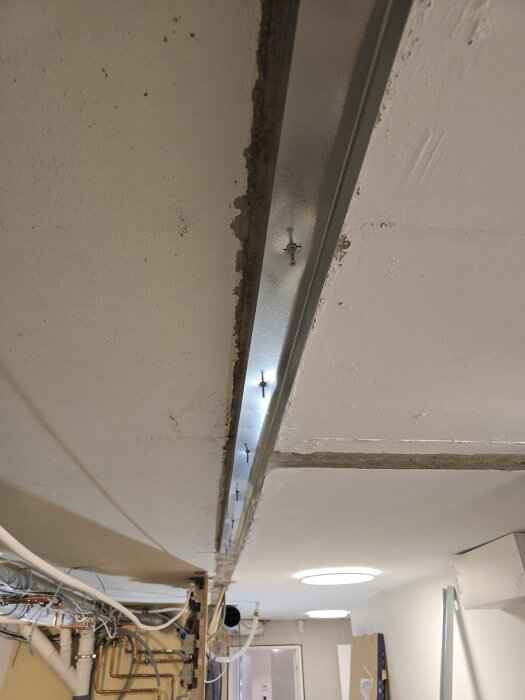 Takskena monterad i taket med spikpluggar. Synliga rör och ledningar längs väggen i ett renoveringsprojekt.