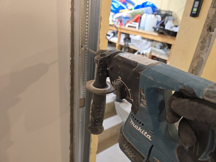 Byggarbetare borrar i vägg för installation av stålregel med Makita borrmaskin, synlig regel och utspritt byggmaterial i bakgrunden.