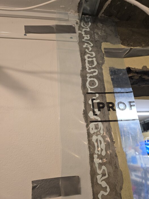 Stålregel och takskena monterade med fogmassa och PE-film, vid en dörröppning under byggprocess av vägg.