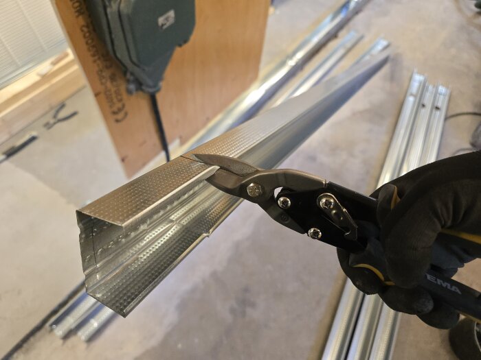 En person klipper en stålregel med en plåtsax i en byggmiljö.