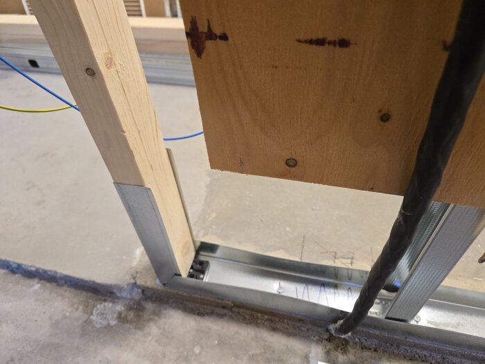 Byggprocess med stålskenor och träregel installerat på betonggolv, med elrör synliga ovanför skenan.