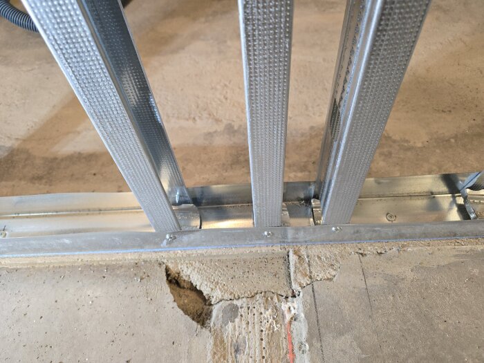 Stålreglar installerade på betonggolv med skenor, del av väggkonstruktion i byggprojekt.