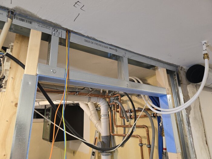 Byggprojekt med stålskenor och reglar längs en vägg, med synliga elrör och ledningar vid taket i ett garage eller förråd.