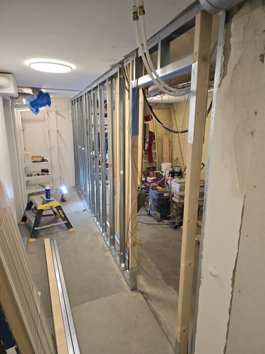 Installation av stålskenor och reglar i rum, påbörjad väggkonstruktion med synliga trä- och stålhållare samt kabeldragning i byggprojekt.