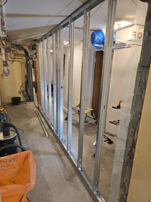 Byggprojekt med stålreglar uppsatta på en vägg i ett garage, med verktyg och byggmaterial synligt runtom.