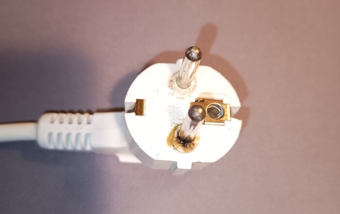 Överhettad stickpropp med glappkontakt, visar begynnande skador och potentiell brandrisk.