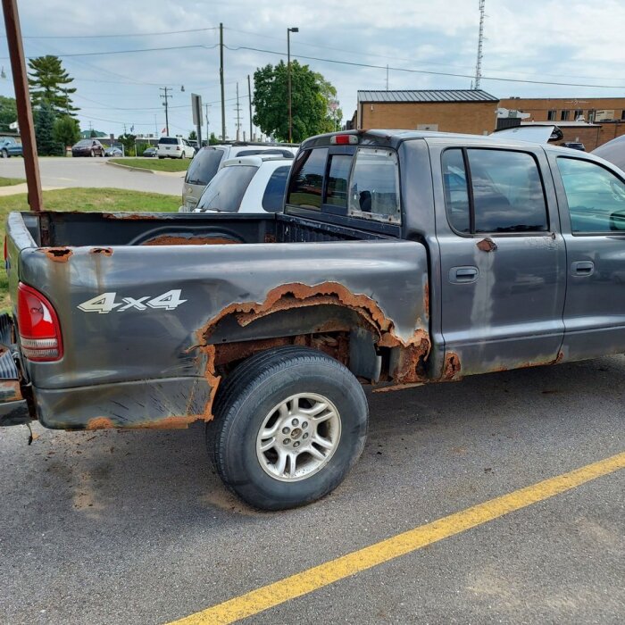 Grå pickup med omfattande rostskador på karossen, parkerad på en asfalterad yta.