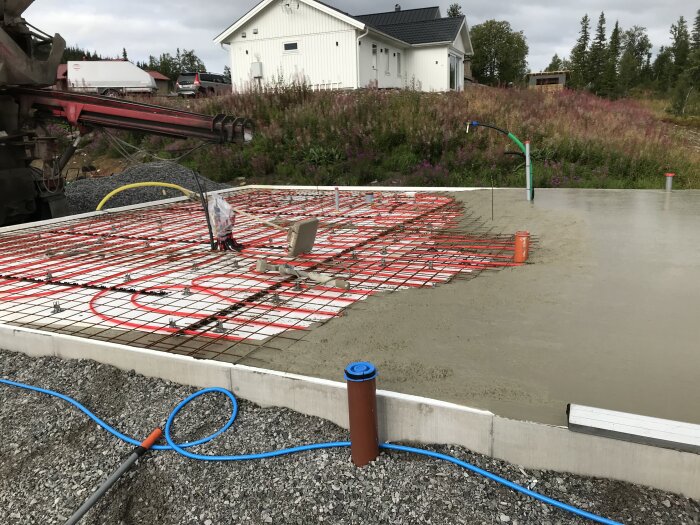 Fritidshusets grund med armeringsnät och rör för avlopp och tilluft. Ett orange tilluftsrör syns i mitten på den nylagda formen.