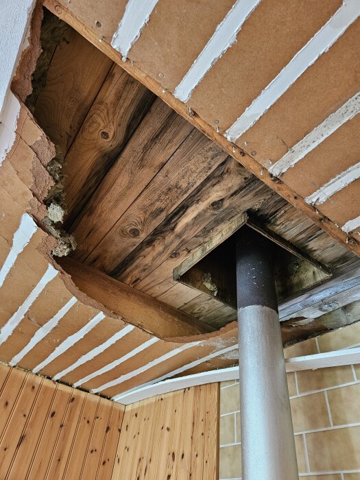 Skadat innertak med synlig isolering och trä, delvis rivet efter läckage. En metallisk rörinstallation passerar genom taket.