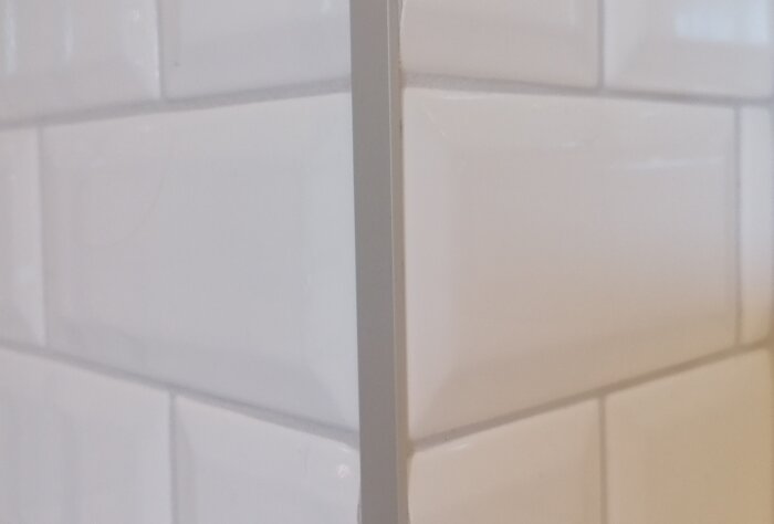Vita kakelplattor monterade runt ett hörn, visar fog och kantdetaljer för badrum eller kök.