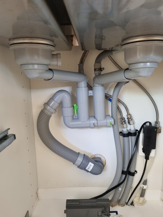 Rörinstallation under diskbänk med flera gråa rör, anslutningar och slangar.