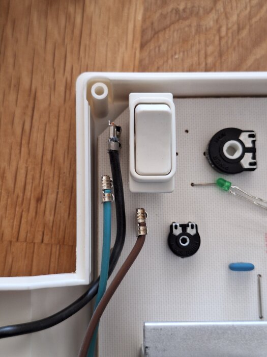 Närbild av en kopplingsbox med en strömbrytare och tre kablar i olika färger (brun, svart och blå), samt komponenter på ett kretskort.