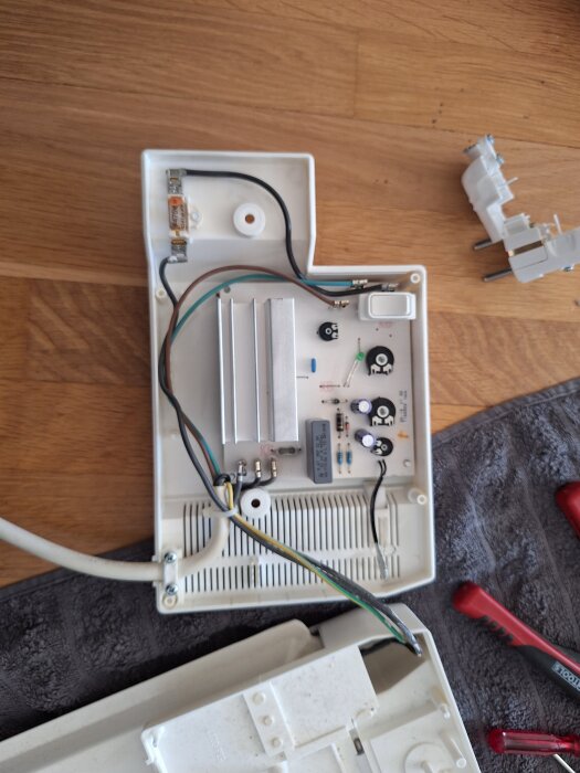 Öppen elbox visar kablar, kretskort och strömbrytare på träbord, stickpropp och verktyg ligger bredvid.