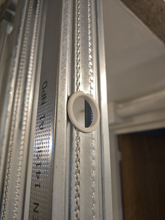 Närbild av stålräls med vit plastgenomföring för flexslangar, använd i byggprojekt för regelväggar och elinstallationer.