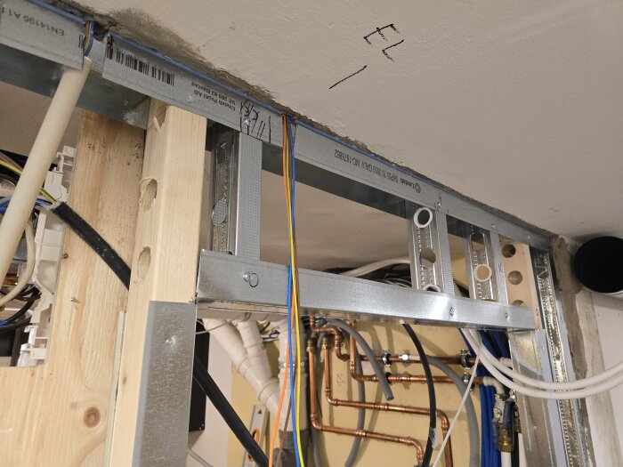 Stålreglar och träreglar med kablar och rör synliga i ett pågående byggprojekt där väggar reglats för installation.