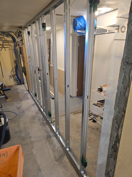 En stålväggsregelstruktur med monterade eldosor i ett renoveringsprojekt, stående på ett betonggolv och omgiven av byggmaterial.