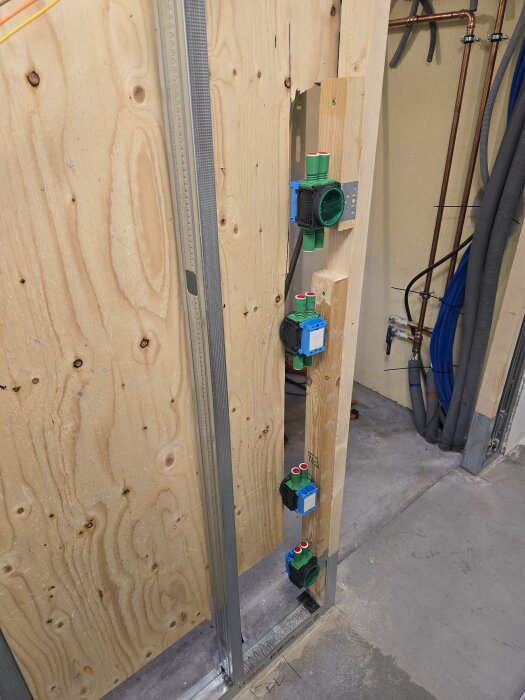 Vägg med trä- och stålreglar, flera eldosor monterade vertikalt på träregeln. Bakgrunden visar olika typer av rör och kablar.