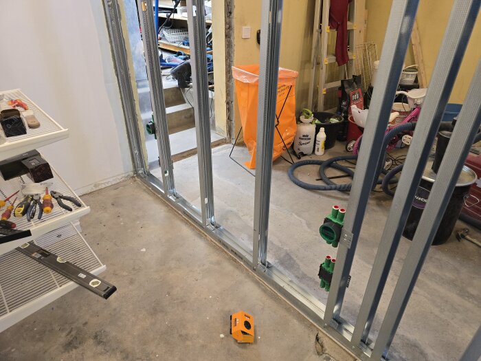 Stålreglar och eldosor framför oorganiserad verktygshylla och byggmaterial i garage eller renoveringsrum.