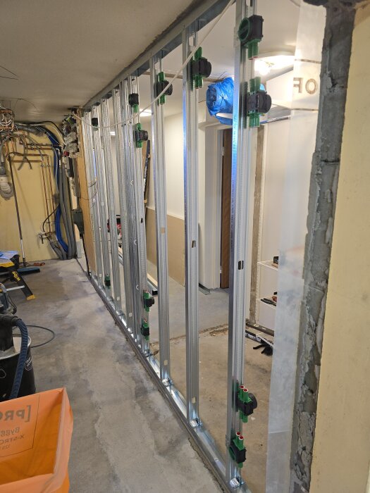 Stålregelvägg under konstruktion med flera eldosor monterade på reglarna, i en inomhusmiljö med synliga rör och en del verktyg.