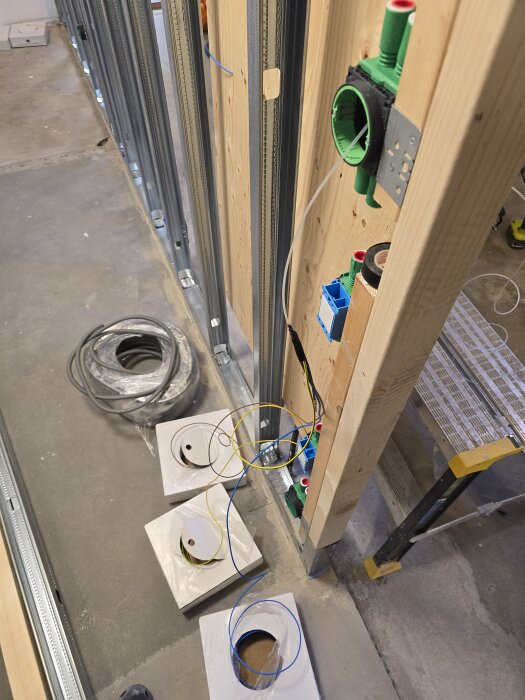 Elektriska installationer i en vägg under byggnation, med kablar, flexslangar och elektriska dosor på en regelvägg av trä och stål.