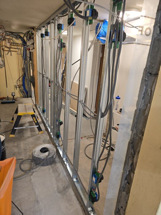 Vägg med stålskenor och kabeldragning, flera flexrör och eldosor synliga, byggmaterial och verktyg i bakgrunden.