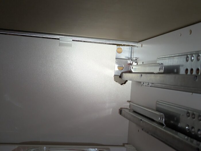 Hål i bakväggen på ett IKEA-skåp orsakat av råttor, synliga metallbeslag runt hålet.