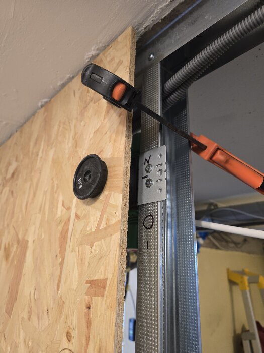 En träskiva monterad på en metallram med tving, omgiven av kablar och byggmaterial, förberedelse för elinstallation.