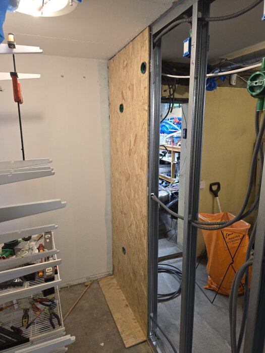 Byggarbetsplats med OSB-skiva monterad på vägg, ventiler och verktyg synliga, samt hyllor med verktyg i förgrunden.