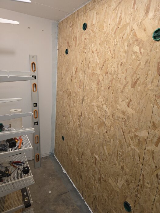 OSB-vägg med gröna uttag monterad, omgiven av verktyg och hyllor, belägen i ett renoveringsutrymme med nivå för vågräta ytor.