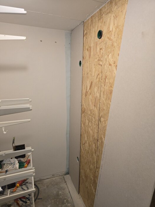 Väggbyggnad med OSB-skivor och gips i en klädkammare; hyllor till vänster; golv och takskenor förbereds.