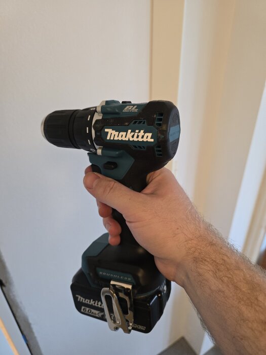 En person håller i en Makita sladdlös borrmaskin mot en vit vägg, använd för projektet att montera och gipsa väggskivor.