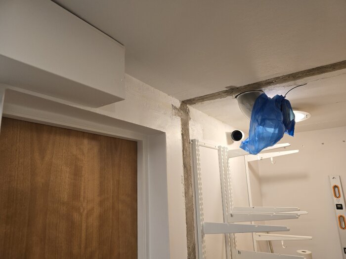 Renovering av klädkammare med monterade hyllor, ventilation, och plastskyddad lampa i taket. En stängd trädörr syns till vänster.