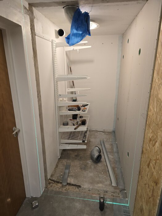 Utrymme för byggprojekt med monterade gipsskivor, stålskenor, och byggverktyg på golv, redo för vidare arbete och installationer.
