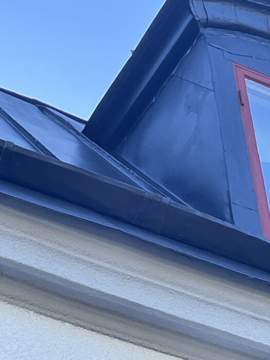 En nymålad plåttakskant med ett fönster och vägg syns under en blå himmel.