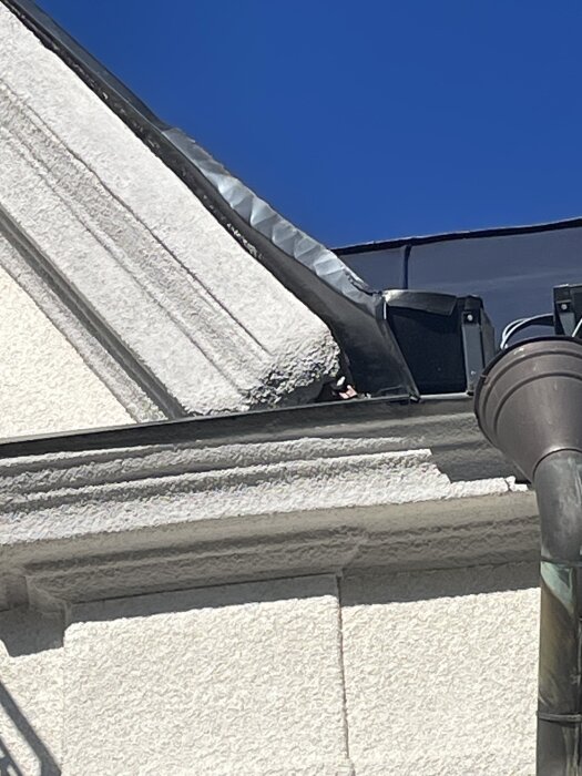 Plåttak nyss ommålat med obruten blå himmel i bakgrunden, närbild på taknock och anslutning mot fasad.