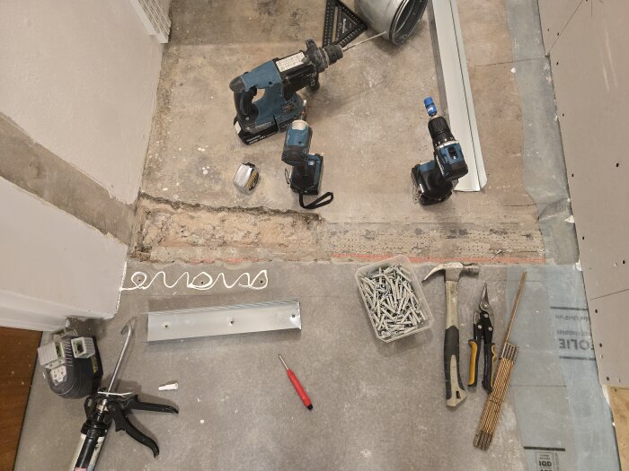 Verktyg och material för byggprojekt ligger på golv, inklusive borr, skruvar, hammare och tätning vid en golvskena.