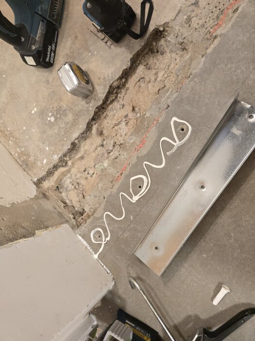 Golv med applicerad bygglim, verktyg och måttband vid sidan, samt en metallprofil för montering.