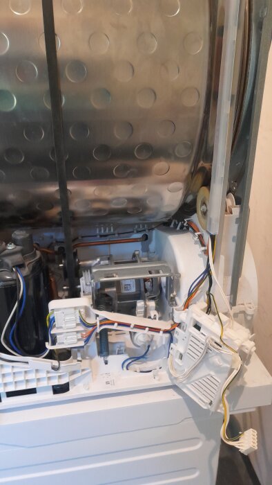 Öppen tvättmaskin visar insidan med trumma, sladdar och komponenter synliga efter byte av motor och spännrulle.
