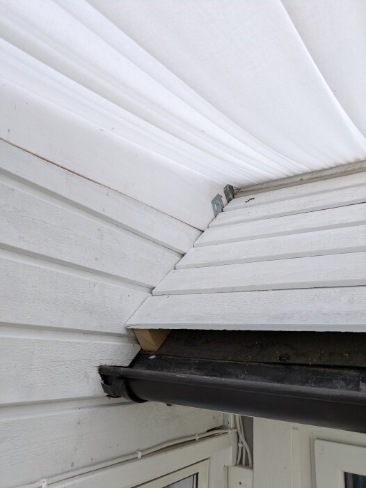 Svart hängränna monterad vid inglasat uterum med vit panel och plåt från taket.