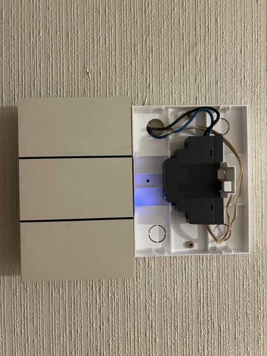 Väggmonterad transformator för dörrlåsinstallation med synliga kablar och en del av enheten utrustad med blått ljus, monterad på strukturerad vägg.