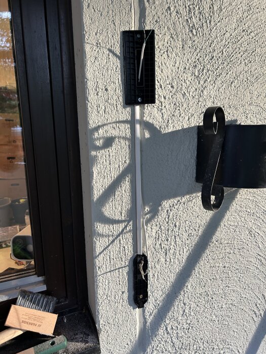 Svart plastmonteringsplatta och kablar på vit husfasad, vid sidan av ett fönster. Verktyg och borste ligger på fönsterkarmen.