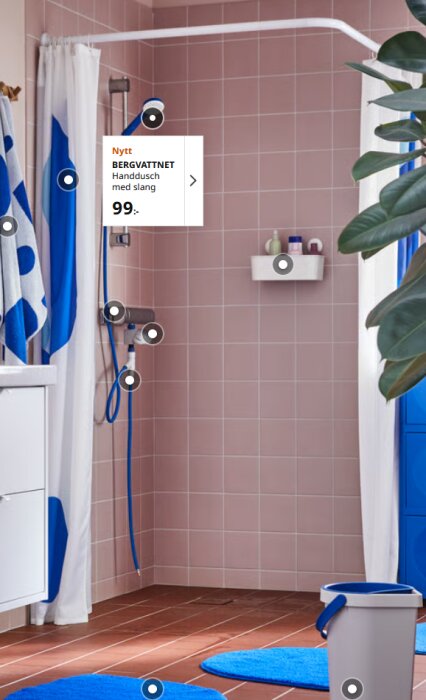 Kakelbeklädd duschhörna med duschdraperi och handdusch. Draperiskena bildar ett U över duschen. Blå detaljer och badrumsmatta syns.